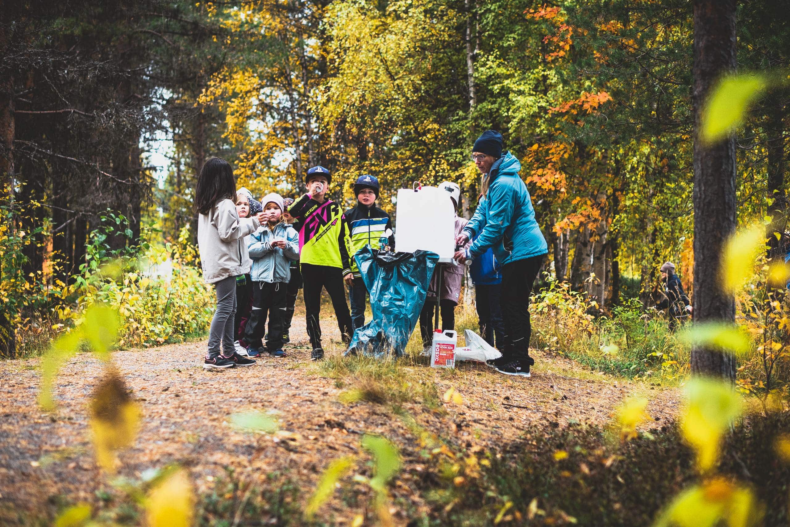 Grupp med barn i skogen. Kvinna undervisar dem. 